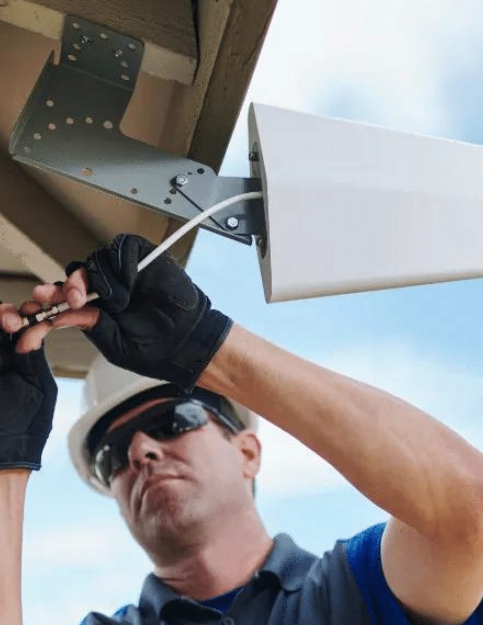 Technician in a hard hat installing a cell booster antenna under a roof overhang